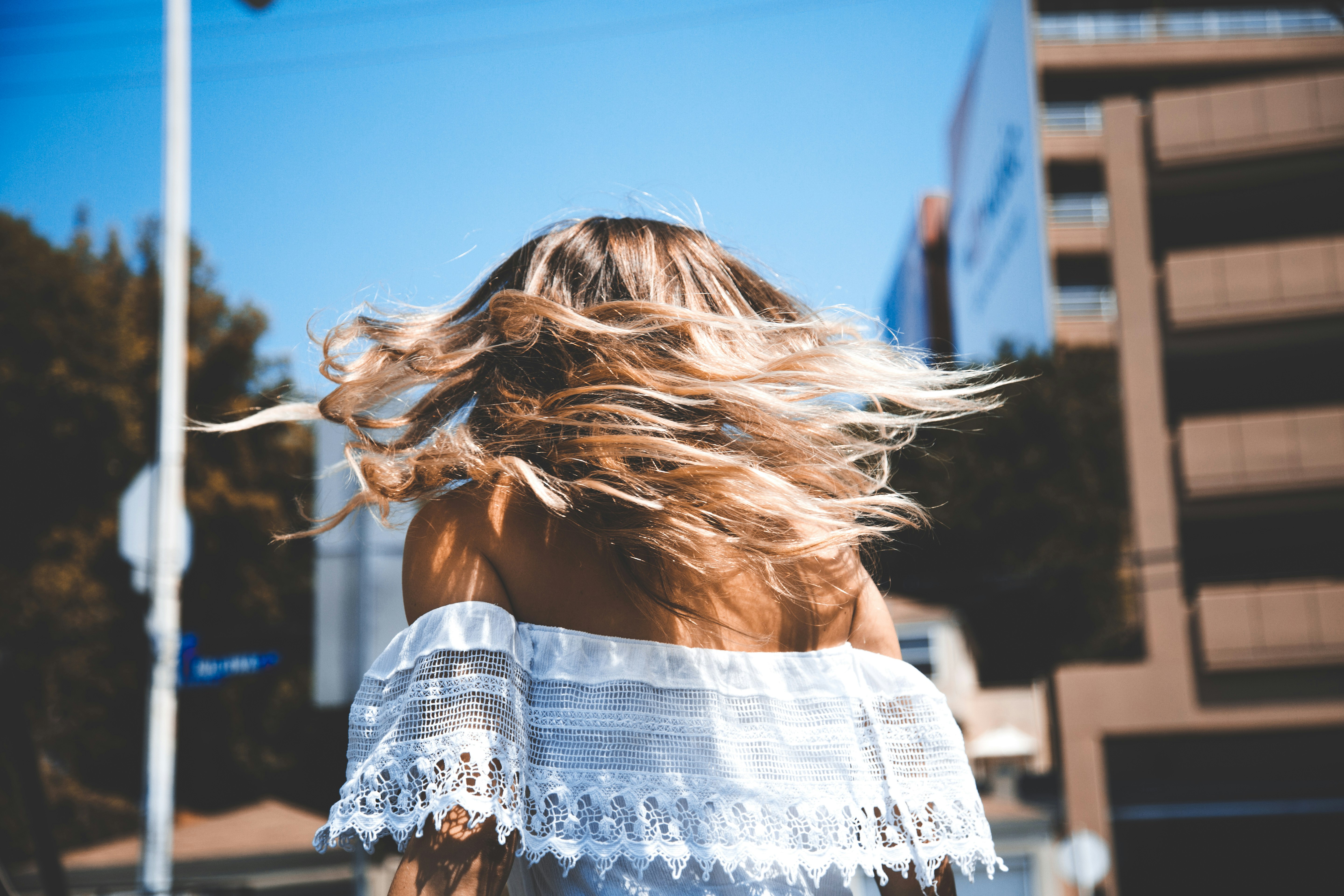 photo of woman wearing white off-shoulder crop top standing beside concrete building under clear blue sky